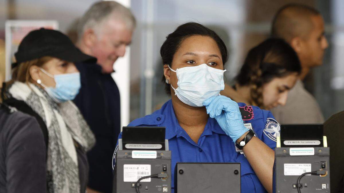 A Transportation Security Administration (TSA) employee adjusts her face mask while screening passengers entering through a checkpoint at John F. Kennedy International Airport, Saturday, March 14, 2020, in New York. The American Academy of Family Physicians recommends workers without insurance contact a local health department or community health center for help. (AP Photo/Kathy Willens)