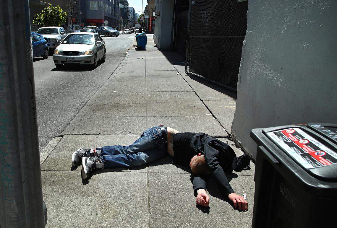 A man lies on the sidewalk beside a recyclable trash bin in San Francisco. San Francisco may have hit peak saturation with tent camps, stinky urine and trash littering its filthy streets.