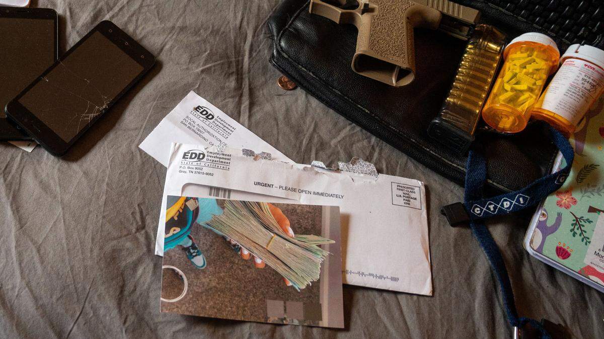 Items collected in Arden Arcade during a 2021 Sacramento County investigation targeting California Employment Development Department fraud include two EDD applications for unemployment insurance payments, more than 100 Xanax tablets with no prescription, fake ID cards, nearly $2,000 in cash and a ghost gun with no serial number. A page in the notebook nearby reads “Fraud Bible/Methods.”