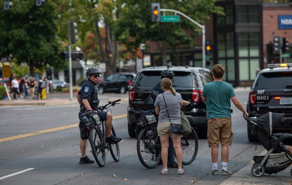 Two Sacramento Police bicycle officers speak with bystanders about the closure of the intersection of Broadway and Land Park Drive for dueling protests about police funding and homelessness on Saturday.