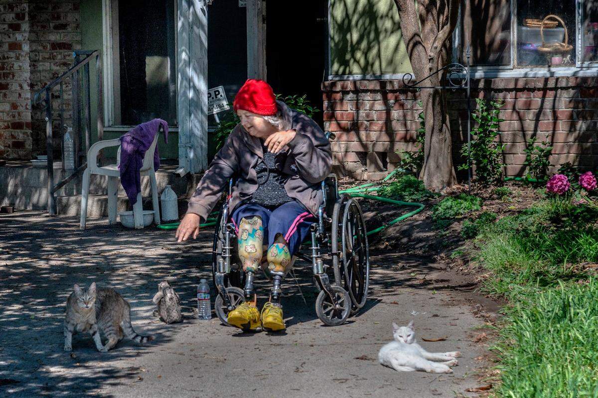 Linda Siegrist, 68, sits outside in the sun with two of her cats in Sacramento in March. Siegrist, a double amputee who suffers from diabetes and other healthcare issues, finds comfort in her cats as she waits outside for Dan Collins to come and inspect her home that is in receivership. The Bay Area Receivership Group has charged five times in fees than what it spent on doing work on the house.