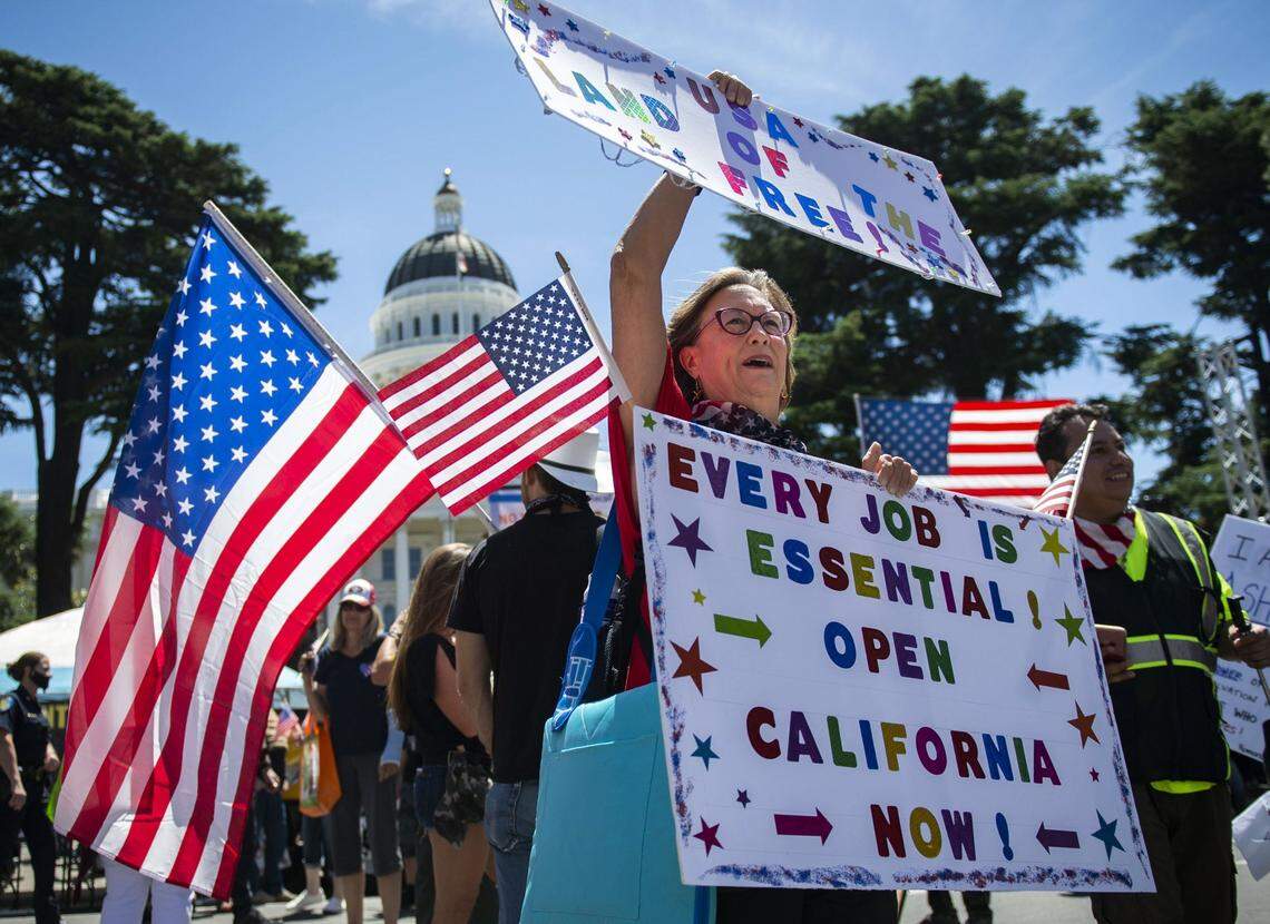 Carol Ball of Richmond holds up her homemade signs in front of the west steps of the state Capitol in downtown Sacramento on Saturday, May 23, 2020, as protesters gathered at Liberty Fest to protest Gov. Gavin Newsom’s stay-at-home order.