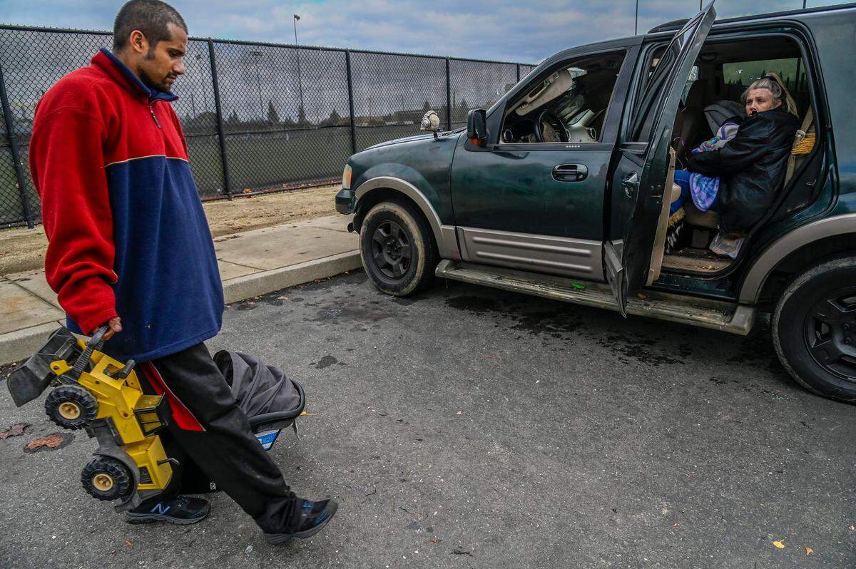 Alfredo Gonzales, 30, carries a toy truck one of his children was playing with at a park in Rancho Cordova on Thursday, Dec. 9, 2021, while Geri Wells nurses their baby Orion in the SUV they live in because their motorhome was towed away by the city last month.
