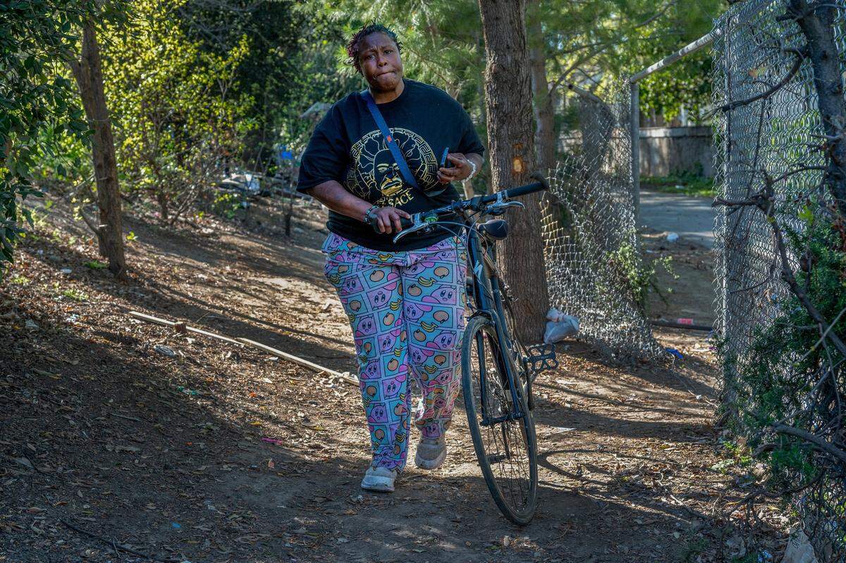 Elizabeth Williams pushes her bicycle past a hole in a fence as she heads out on March 26 to get groceries to cook dinner at the same homeless encampment in South Natomas where she was arrested in February and jailed for a day.