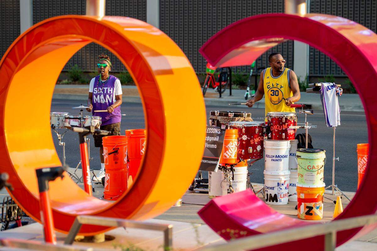 Quincia Lynn, left, and Brian Jackson Jr., seen through a DoCo sign, perform at the corner of L and 5th streets during the Sacramento Kings first preseason game on Oct. 4 at Golden 1 Center in downtown Sacramento.