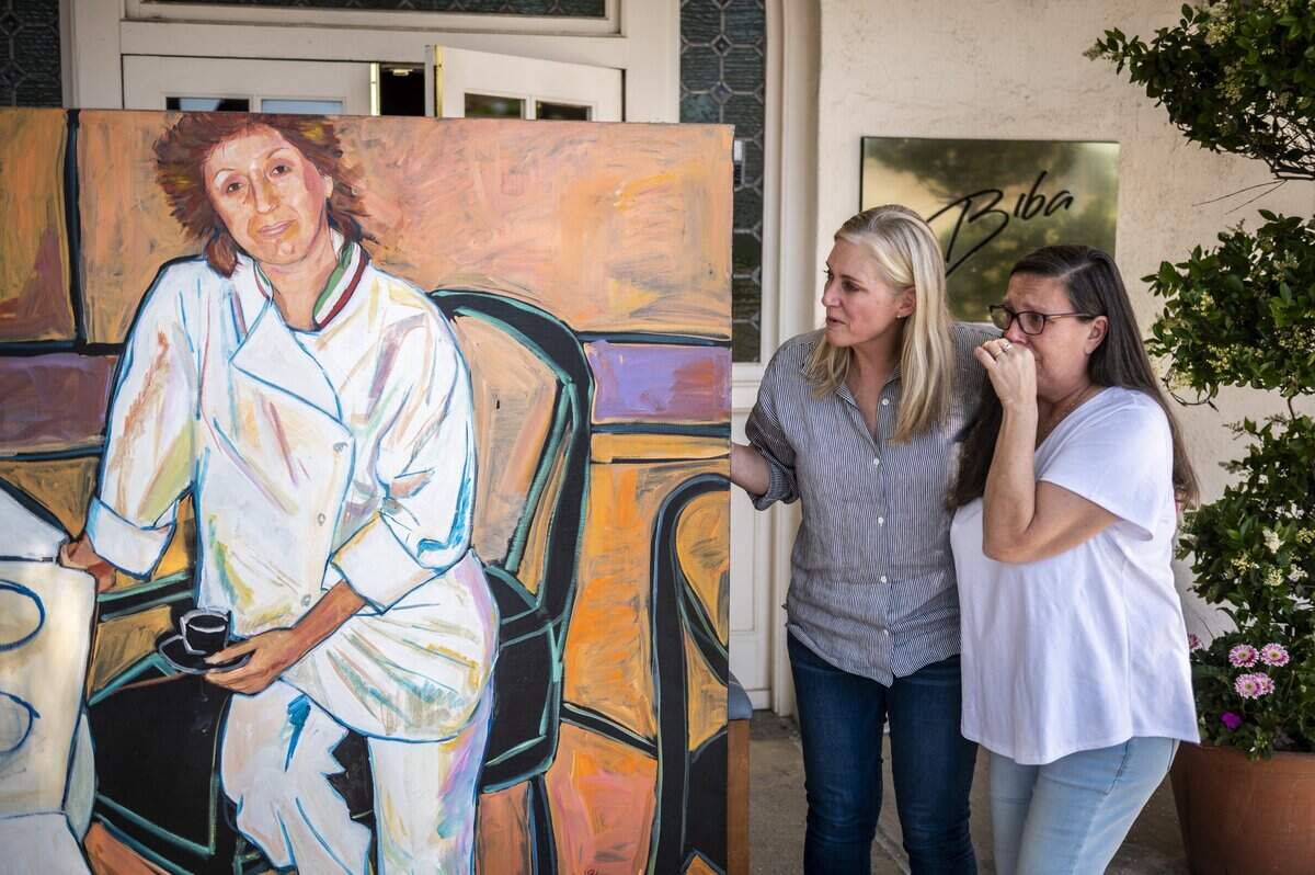 Carla Caggiano Elkins, right, and Paola Caggiano McNamara, daughters of the late Biba Caggiano, get emotional while looking at a painting of their mother that had been moved outside her namesake restaurant for a staff portrait on Sunday, May 3, 2020.
