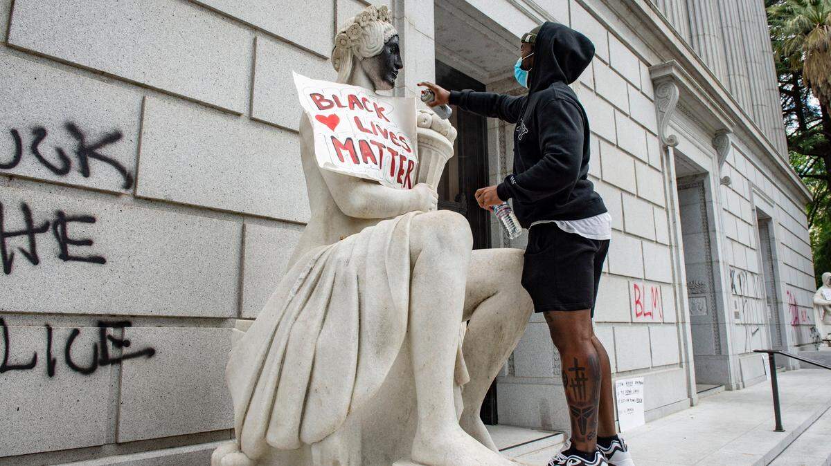 A protester spray paints a statue in front of the California State Library in downtown Sacramento on Saturday, May 30, 2020.