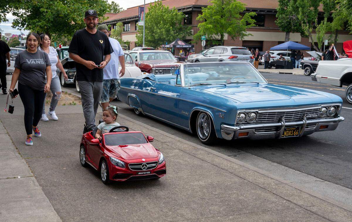 Camil Maciel 18 months, rides in a remote-controlled car powered by her dad, Jose Maciel, and followed by mom, Liliana Alejo as they walk to see the lowriders cruise down Broadway on Saturday.