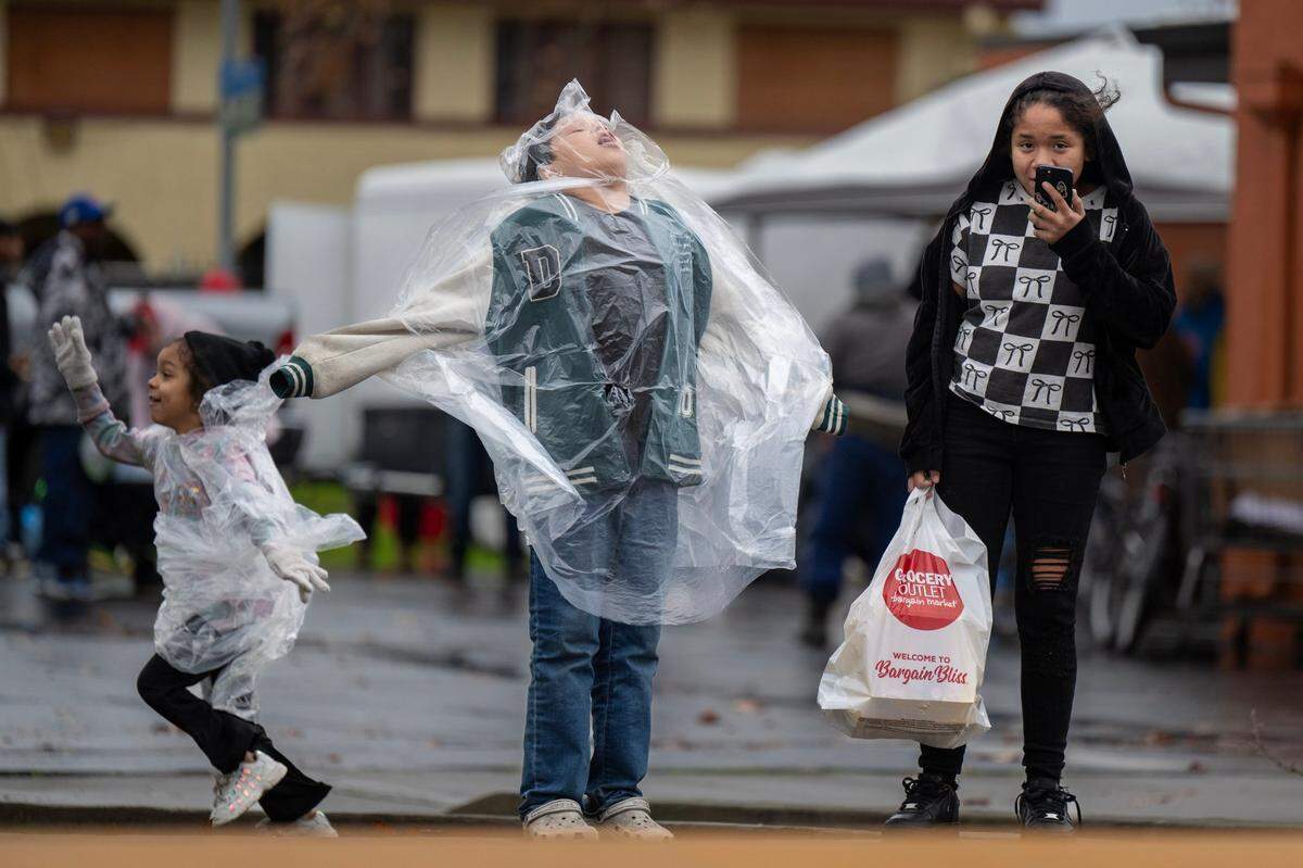 David Sinohui, center, weathers the wind and rain with his sisters Lienna, right, and Abigale as they wait for their grandmother to cross the street in Del Paso Heights on Saturday, Dec. 13, 2024.