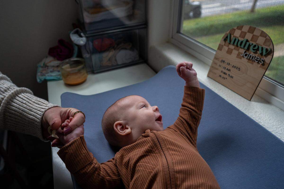 Michelle Glass holds the hand of her 2-month-old son, Andrew James Glass, on a changing table as he smiles at his handmade birth announcement plaque on Nov. 20 in Rancho Cordova. Andrew was named after his uncle, Andrew James Mathew Pringle, who died in 2023 after being hit by a driver who ran a red light in Rosemont. 