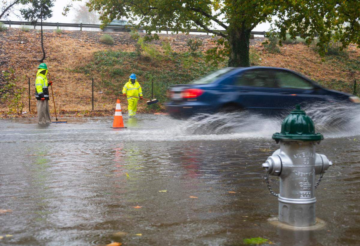 Workers attempt to clear street flooding as cars drive past on X Street in Sacramento during heavy rainfall in 2021. 