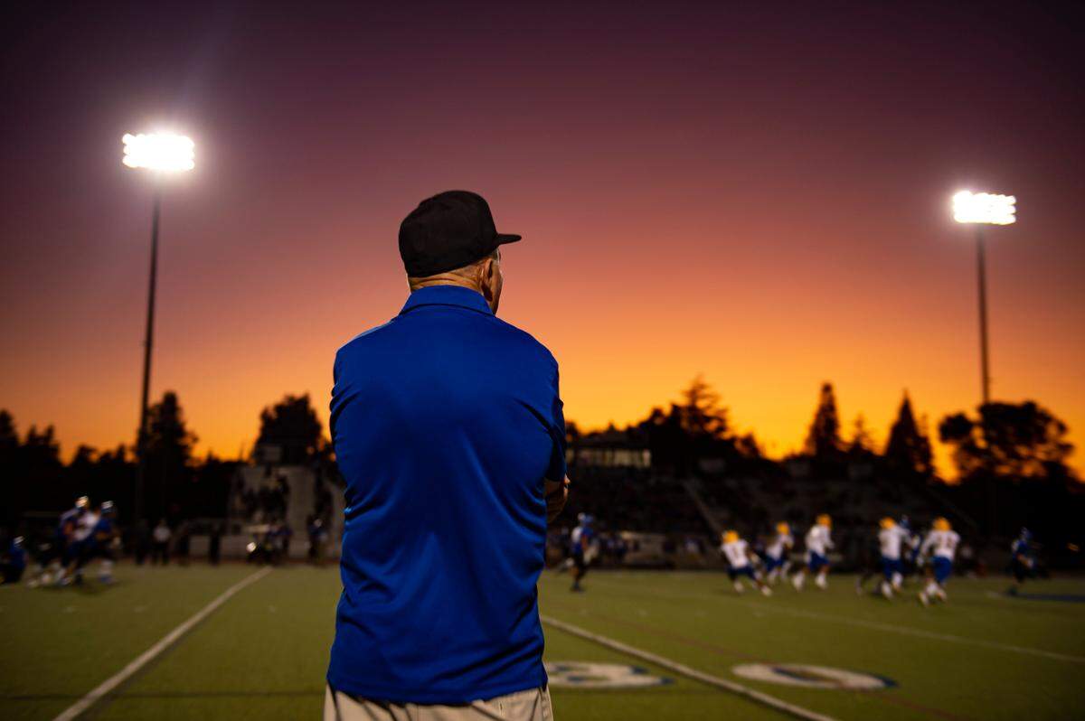 As the sun sets, Grant High School head coach Mike Alberghini stands on the sideline as his team plays at Davis High School in 2019. 