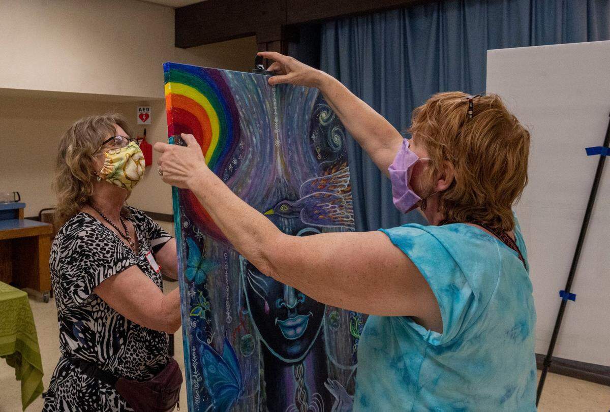 Maureen Dion-Perry, left, helps artist Sara J Morgan set up her painting at the “Standing Against Racism with Art” show held by the Civil Rights Now group in Placerville, on Friday. “This is the first time ever showing my artwork in public, and I felt inspired and unified by all the art here at a show in our town,” said Morgan, who brought her piece at the last minute after seeing the other work.