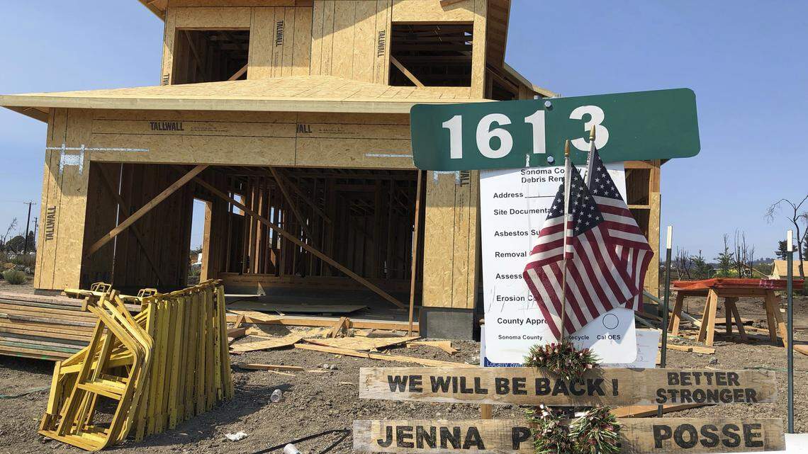 In this Friday, August 10, 2018, photo, signs and flags mark the partially rebuild home of Debbie and Rick Serdin in the Coffey Park neighborhood of Santa Rosa, Calif. The Trump administration’s tariffs have raised the cost of imported lumber, drywall, nails and other key construction materials, squeezing homeowners who seek to rebuild quickly after losing their houses to natural disasters, such as the wildfires that destroyed Coffey Park. (AP Photo/Jonathan J. Cooper)