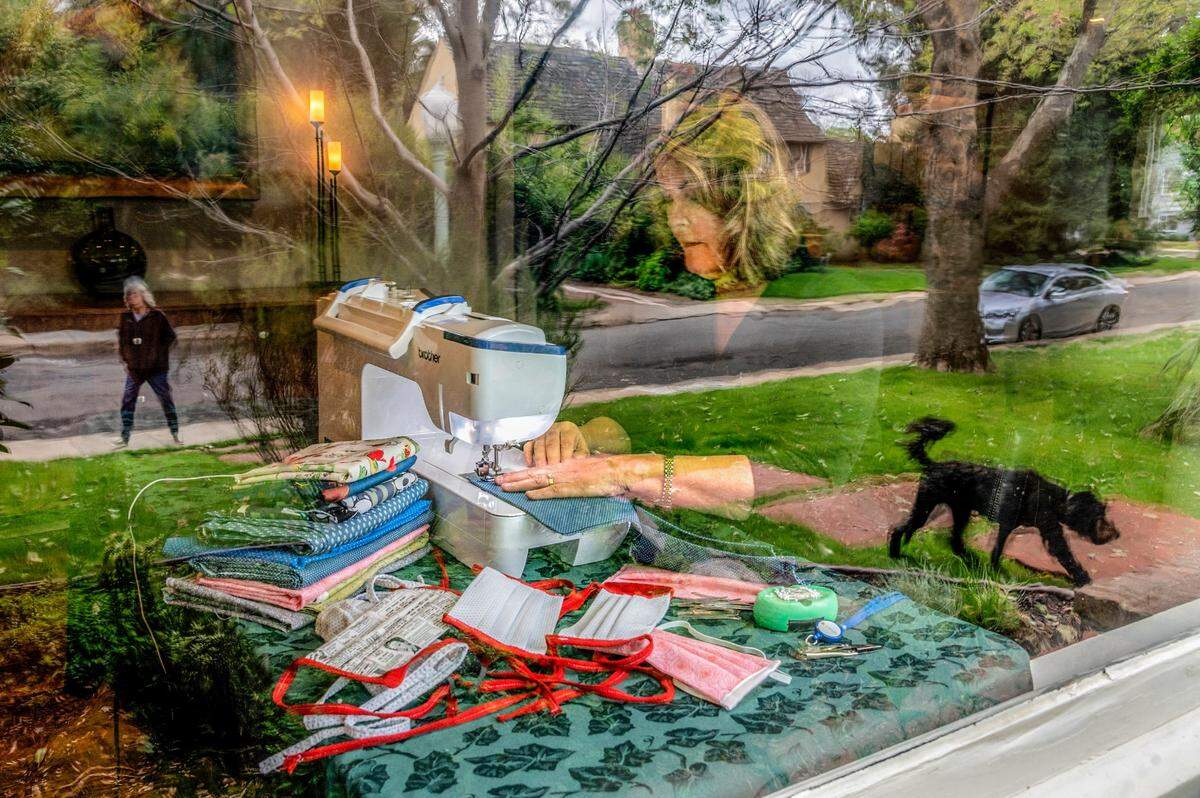 Brenda Fotos sews masks to donate to area hospitals in her living room as a neighbor walking her dog is reflected in the window in the Curtis Park neighborhood of Sacramento on Thursday, April 9, 2020. Fotos is one of several members of the Sacramento chapter of the American Sewing Guild making masks to help keep medical workers safe during the coronavirus pandemic.
