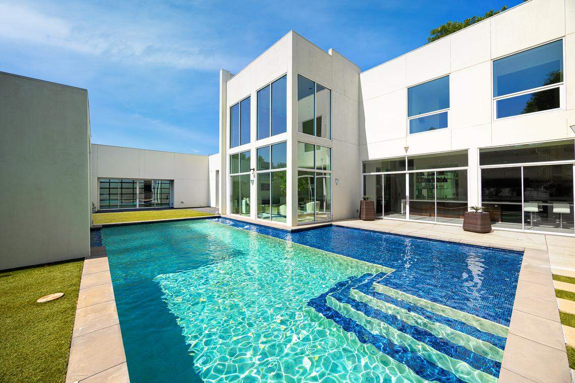 Expansive floor-to-ceiling glass doors connect the light-filled interior to the resort-inspired backyard, where a pool, spa, outdoor kitchen, firepit, and projection wall create the ultimate setting for gatherings.