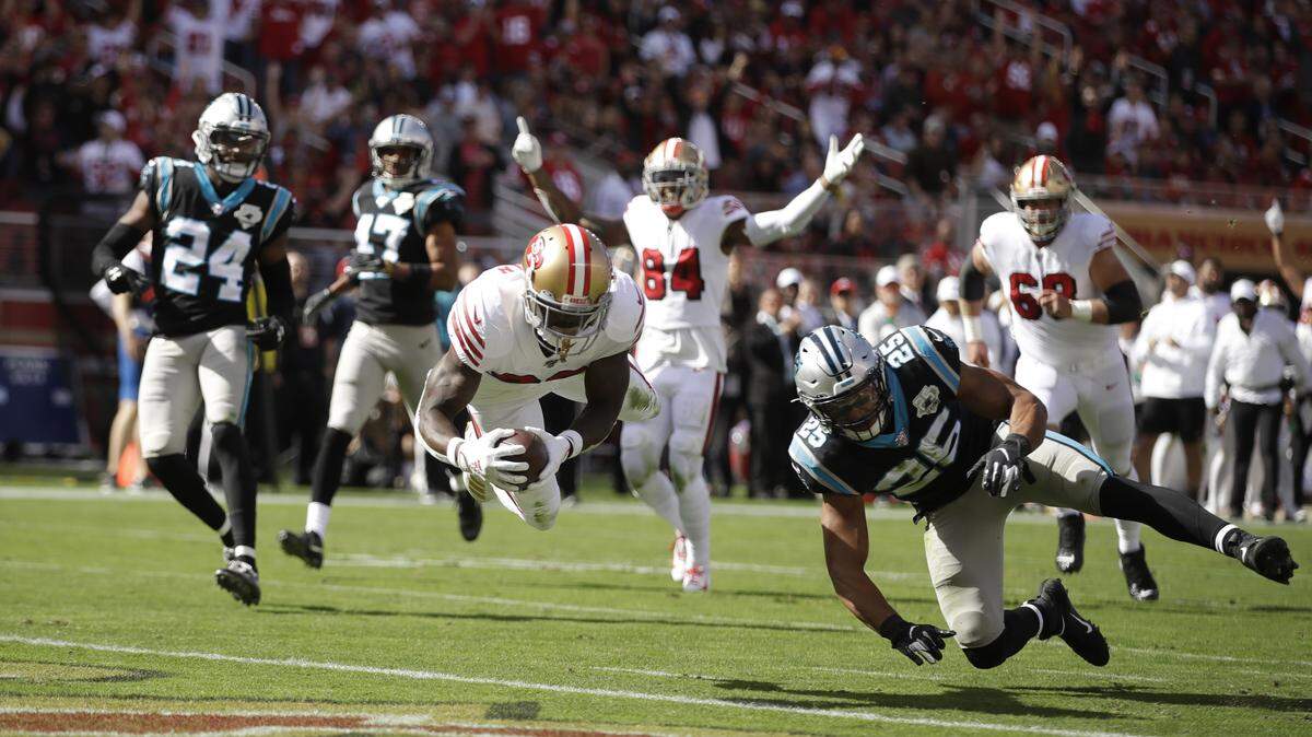 San Francisco 49ers running back Tevin Coleman goes diving into the end zone to score a touchdown as Carolina Panthers strong safety Eric Reid (25) and cornerback James Bradberry (24) look on during the first half of an NFL football game in Santa Clara, Calif., Sunday, Oct. 27, 2019. In the background is San Francisco 49ers wide receiver Kendrick Bourne (84). (AP Photo/Ben Margot)