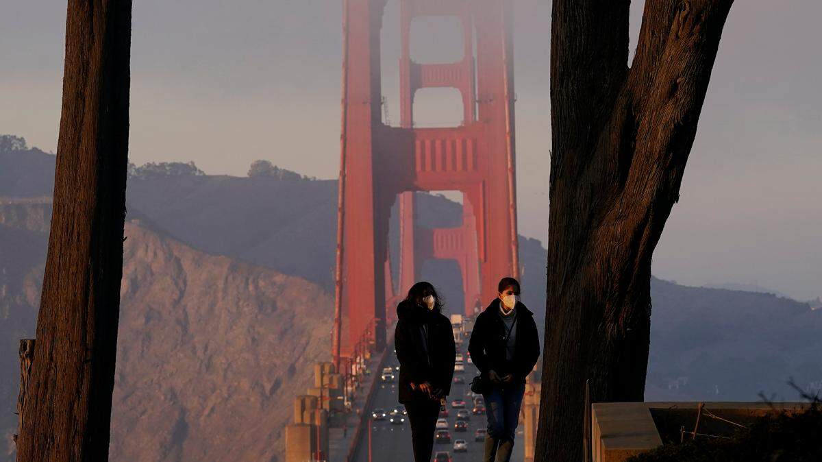 FILE - In this Dec. 21, 2020, file photo, people wear face masks while walking up stairs at the Golden Gate Overlook in the Presidio in front of traffic driving on the Golden Gate Bridge in San Francisco. California, for decades a symbol of boundless growth and opportunity that attracted people from across the U.S. and abroad, has stagnated.