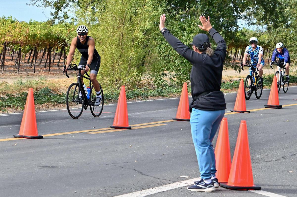 Valerie Saguin, of Los Angeles, waves as her husband, Jeffrey Saguin, passes at about the 38-mile marker on the bike course during the Ironman California triathlon on Sunday.