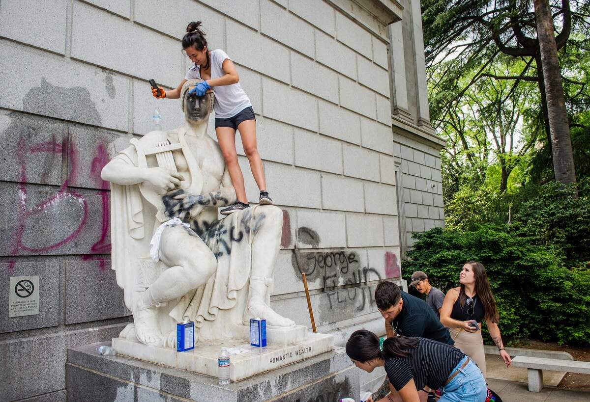 23. Elisabeth DeLeon of Sacramento scrubs a statue on Sunday, May 31, 2020, in front of the California State Library on Capitol Mall that was defaced with graffiti following the Saturday protest of the death of George Floyd.