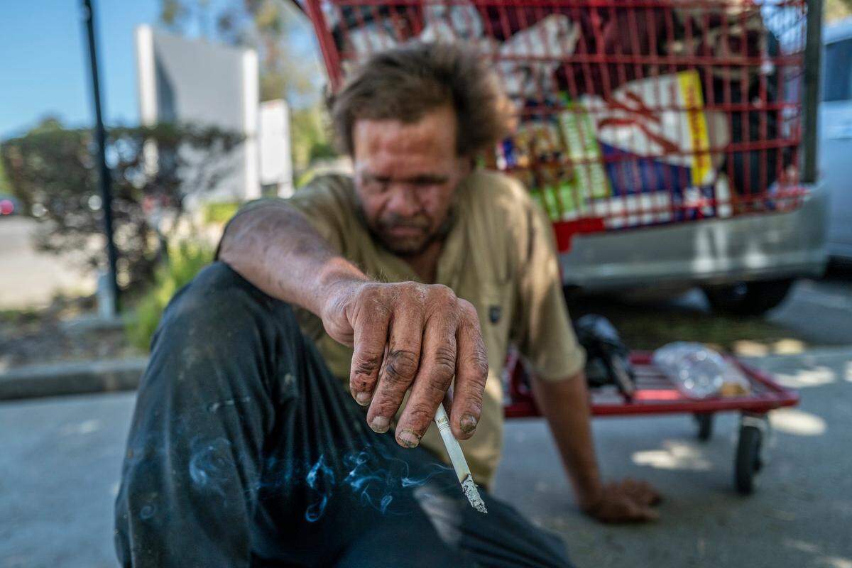 Mark Rippee, 59, who is blind, rests on the ground holding a cigarette in Vacaville on July 27. He said he needs someone to give him a ride to look for apartments and a job.