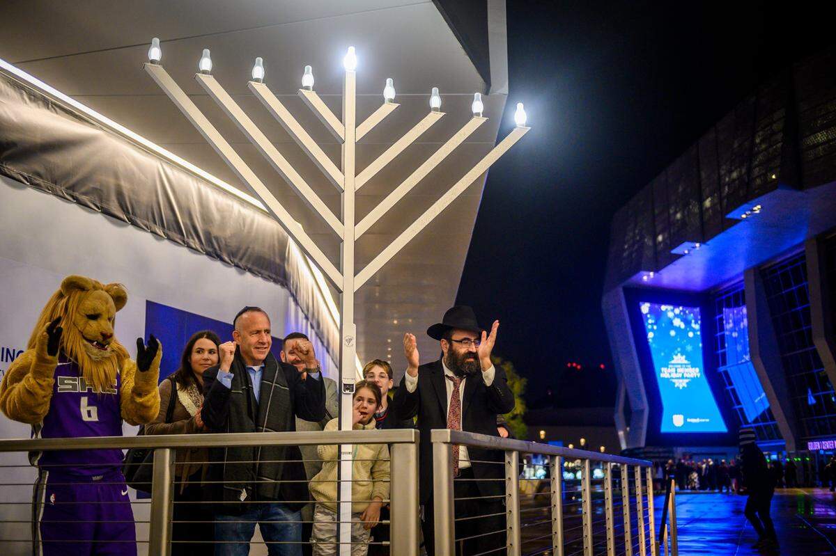 Sacramento Mayor Darrell Steinberg, Rabbi Mendy Cohen and the Sacramento Kings mascot Slamson the Lion celebrate after lighting a menorah at Downtown Commons in Sacramento on Dec. 22, 2019.