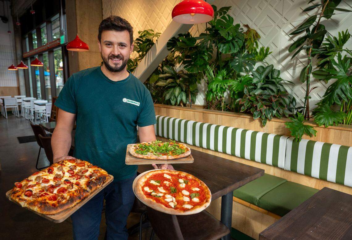 Owner Juanes Ramazzini holds three styles of pizzas earlier this month at Bambina’s Pizza and Pasta, which opened recently in midtown’s Ice Blocks development.