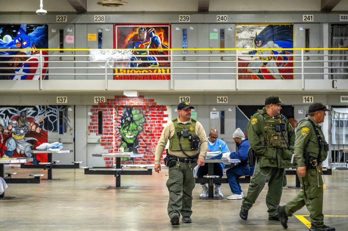 Correctional Officer Thomas Grady, left, with the Salinas Valley Resource Team, walks last month through B Ward, where murals of comic book characters adorn the walls of the maximum security prison. The murals are part of the prison’s larger effort to make facilities more humane. Normalization is a key pillar of the California Model.