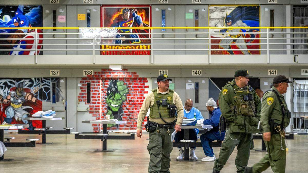 Correctional Officer Thomas Grady, left, with the Salinas Valley Resource Team, walks through B Ward on March 6, 2025, where murals of comic book characters adorn the walls of the maximum security prison. Advocates and a federal judge hope thousands of dollars in bonuses will help California prisons finally attract and keep sufficient levels of mental health staffing.
