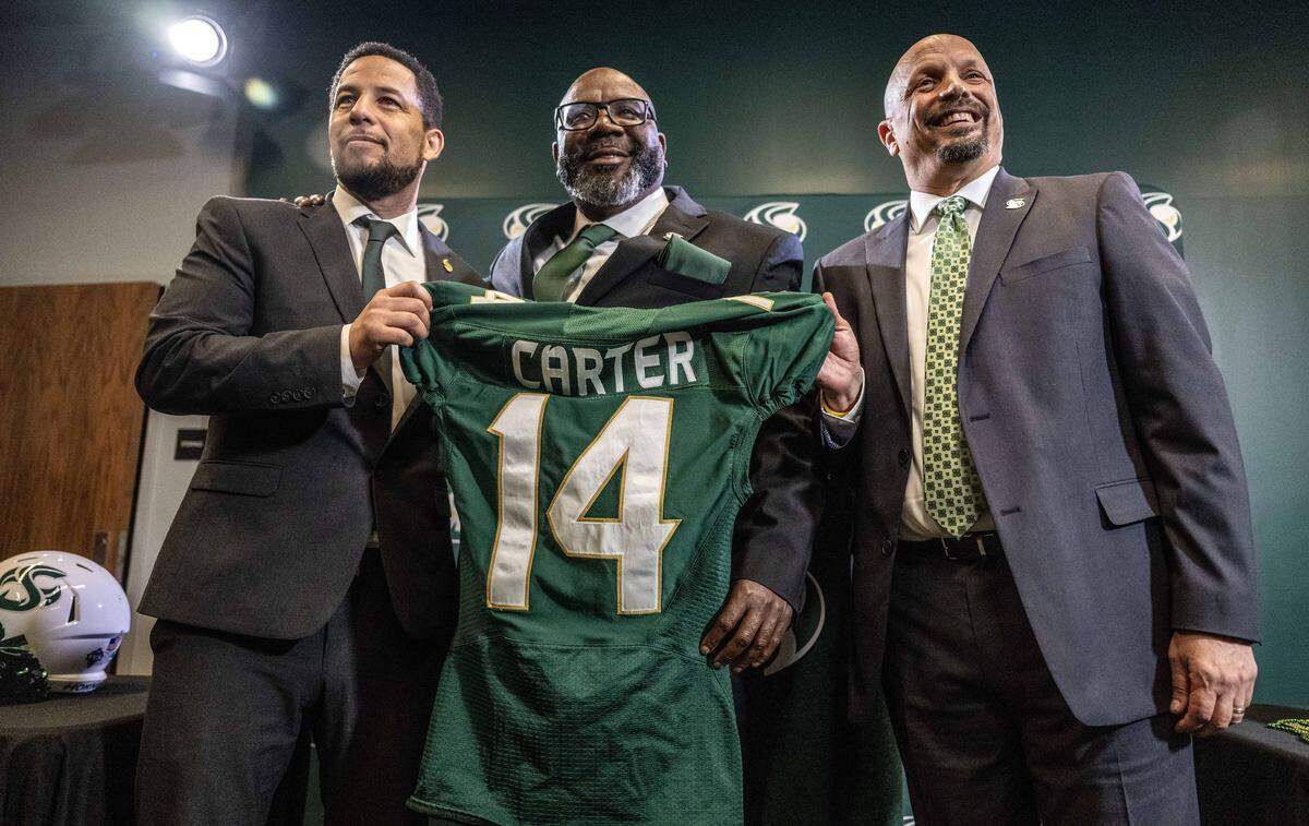 New Sacramento State football coach Alonzo Carter holds a No. 14 jersey as he stands with university president Luke Wood, left, and athletic director Mark Orr during his introductory news conference on Thursday. Carter is the school’s 14th head football coach. 