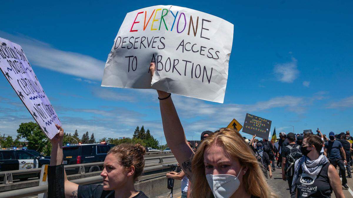 Abortion rights protesters hold signs on the northbound Interstate 5 on-ramp in downtown Sacramento on Monday, July 4, 2022, police vehicles behind them mark the start of traffic stopped on the freeway.