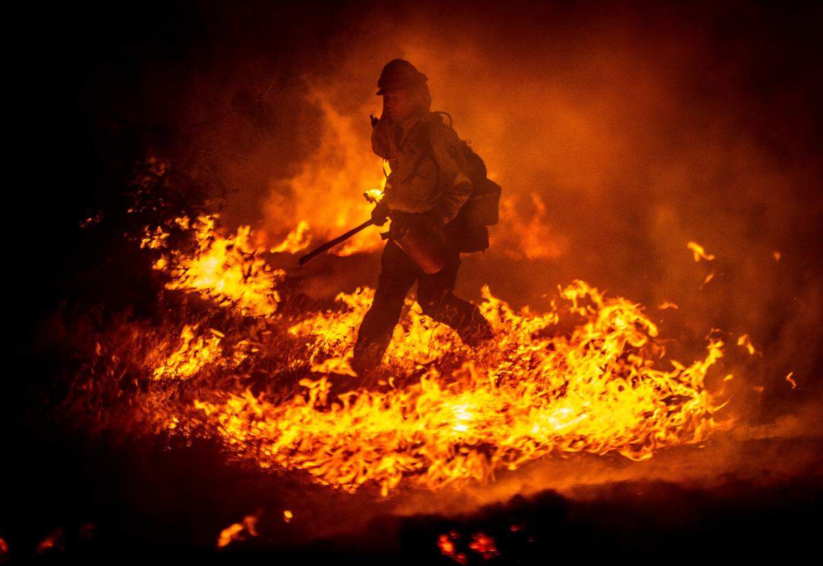 A CalFire firefighter jumps over some flames at the Sites Fire in Colusa County on Sunday, August 2, 2020.