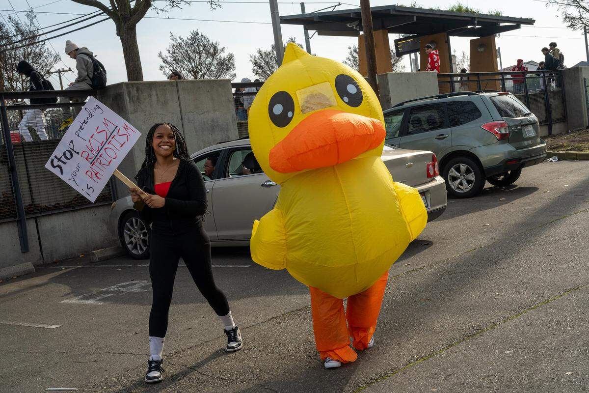 Nalaya Harrell holds a sign alongside Lola Morado, dressed in a duck costume, as they join McClatchy High students catching light rail during a districtwide walkout on Friday in Sacramento, part of a nationwide student effort to protest immigration enforcement following fatal shootings in Minneapolis.