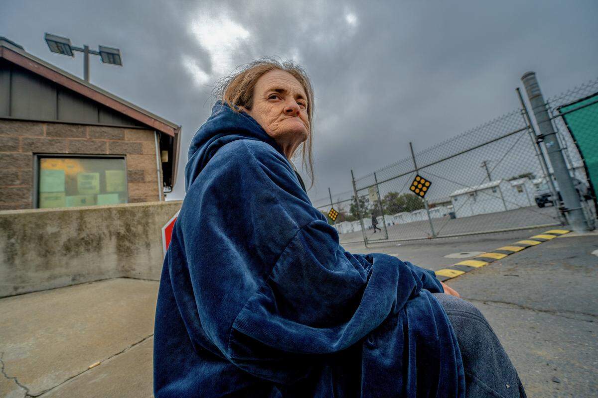 Susan Alhaqq, 54, rests outside the guard building at the Roseville Road shelter in Sacramento on Dec. 5. She moved there after the city shut down Camp Resolution, the self-governing encampment where she had lived. Alhaqq, who is still waiting for permanent housing after a year and a half, feels the shelter operates like a jail with searches and strict rules.