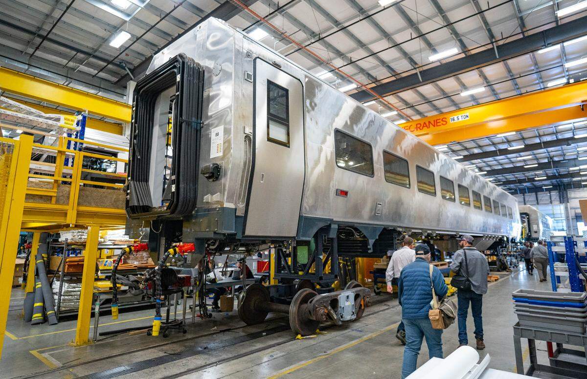 People walk by an unfinished Amtrak Airo car during a tour of the Siemens manufacturing facility on in October. The company plans to start delivering 87 train sets to the passenger service by the end 2024.