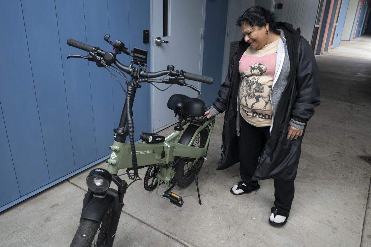 Anna Crespo, 55, fondly pats her e-bike as she stands in her apartment complex in  Sacramento on Thursday.