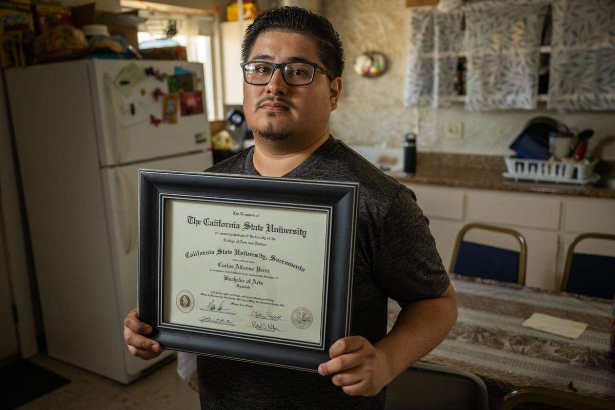 Carlos Alfonso Perez holds his college diploma from Sacramento State on in August. Perez is midway through his master’s program and still wakes up early to work in the field with his farmworker family.