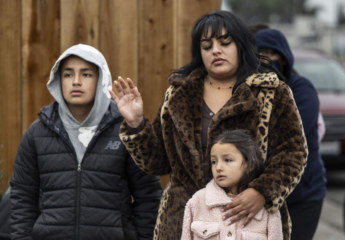 Adriana Hernandez raises her hand in prayer with her children during a vigil on Sunday for the four people killed and 11 injured after a mass shooting near Stockton. 