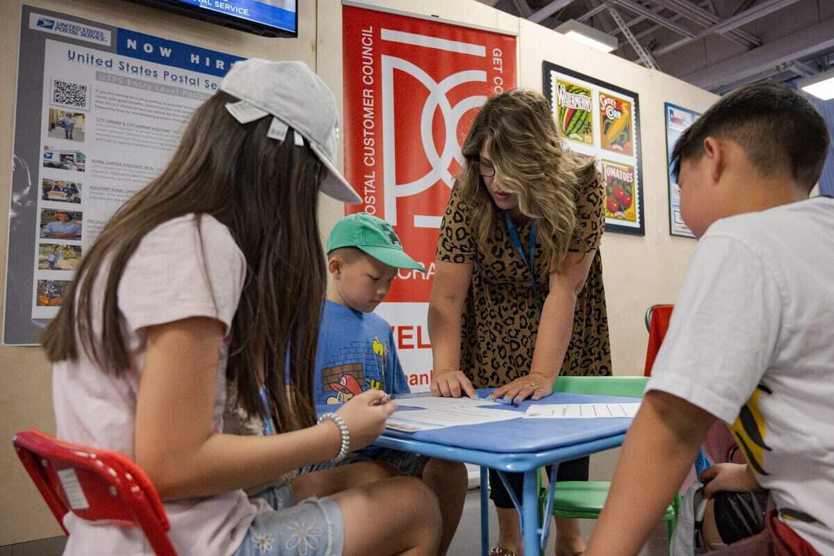 Gina Segura, customer relations coordinator of the U.S. Postal Service, shows the Moua family how to write letters at the post office inside the California State Fair on Tuesday.