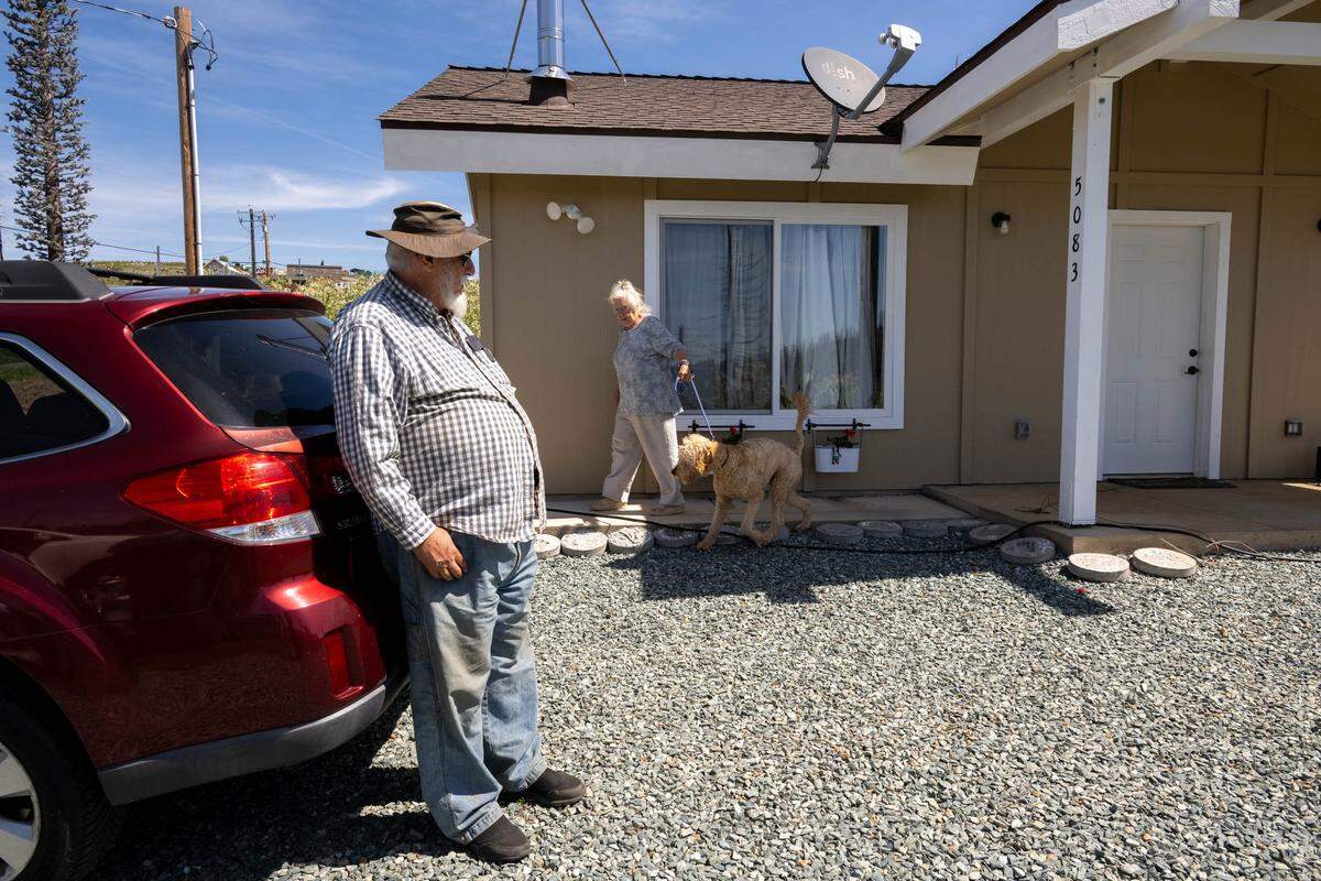 Mac MacNeil, 78, Cathie Adams and their dog Harry stand on May 1 outside their rebuilt 750-square-foot home in Grizzly Flats, which was restored with funding from the Nonprofit Construction Corporation following the 2021 Caldor Fire. The home was built under El Dorado County’s Title 25 ordinance, a streamlined process for smaller owner- or nonprofit-built homes that reduces fees and simplifies requirements.