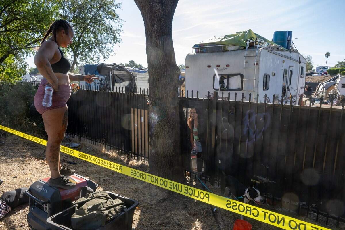 Marie Mowder, a two year Camp Resolution resident, stands on her portable generator outside the fence talking with camp neighbor Jackie Decima as dozens of Sacramento police officers, staffers from the city’s Department of Community Response, and other city workers work to clear Camp Resolution on Monday.