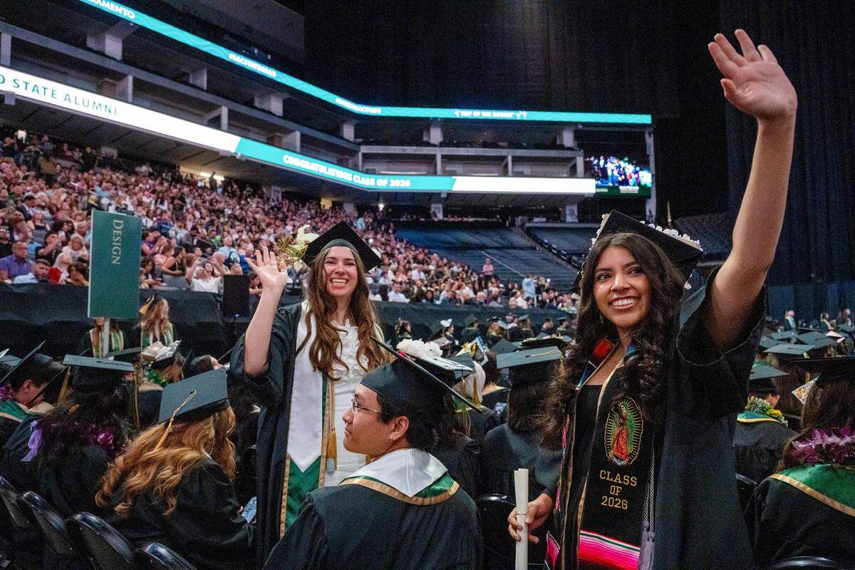 Sacramento State graduates Monce Perez, right, and Lily Nagy, left, wave to family and friends after receiving their diplomas at Golden 1 Center on Friday. They are part of the largest graduation class in the university’s history.