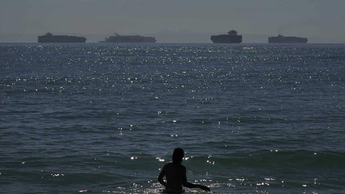 A man wades through the water in Seal Beach on Oct. 1 as container ships wait to dock. Offshore traffic jams have forced ships to wait well beyond their usual zones, dropping enormous anchors near oil platforms and an undersea infrastructure of oil lines.