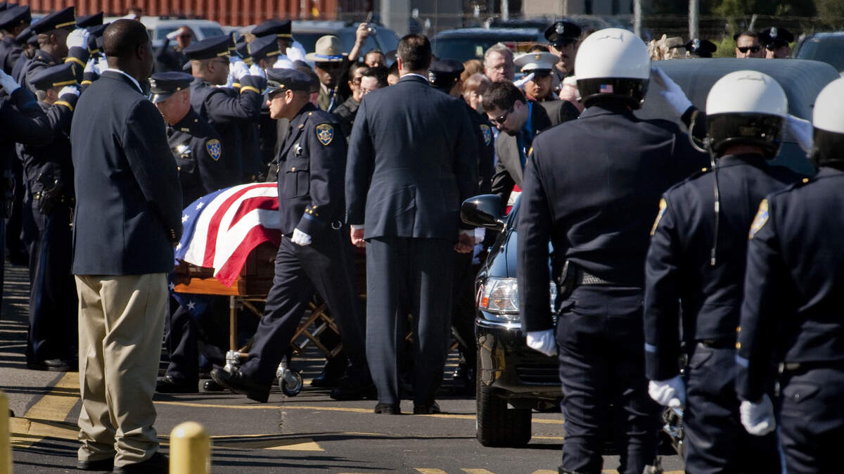 FILE -- Oakland police officers salute as the casket containing the body of a fallen officer is taken into Oracle Arena for a memorial service. Sgt. Mark Dunakin, Sgt. Ervin Romans, Sgt. Daniel Sakai and Officer John Hege were killed in a shooting March 21, 2009. Dunakin’s widowed spouse, Angela Dunakin, died Oct. 28, 2019, following a vehicle crash in Yuba City.