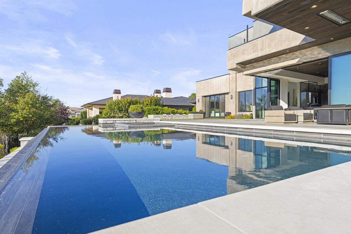 Outside, a private entertainment paradise awaits with a vanishing-edge pool, sitting areas with fire pits, a drop-down screen and projector, and outdoor kitchen with a pizza oven — all of which takes in an expansive view of the second fairway and open sky.