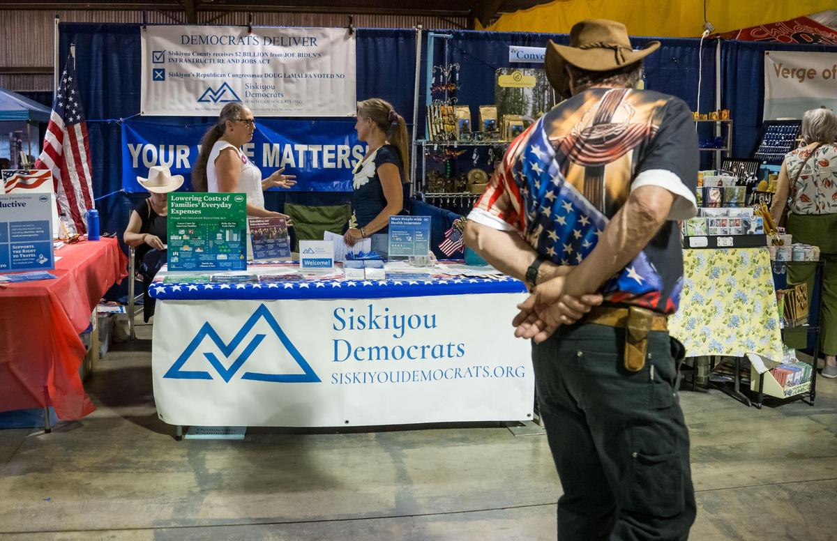 Alice Rogers, left, chair of the Democratic Central Committee of Siskiyou County, and Angelina Cook, a longtime county resident running for the Board of Supervisors, chat while a fair-goer slowly walks past their table at the Siskiyou Golden Fair on Aug. 9, 2023, in Yreka.