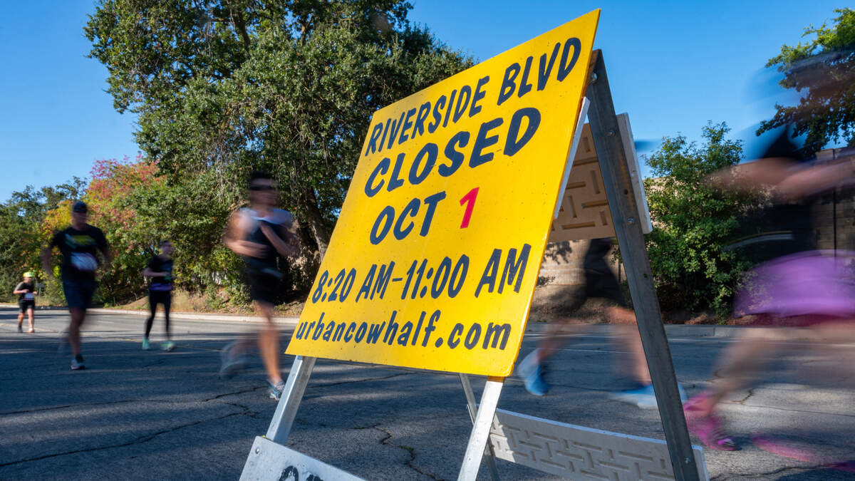Runners whiz by a road closure sign on Riverside Boulevard in Sacramento during the Urban Cow half marathon last year. This year's race will close roads on Sunday.