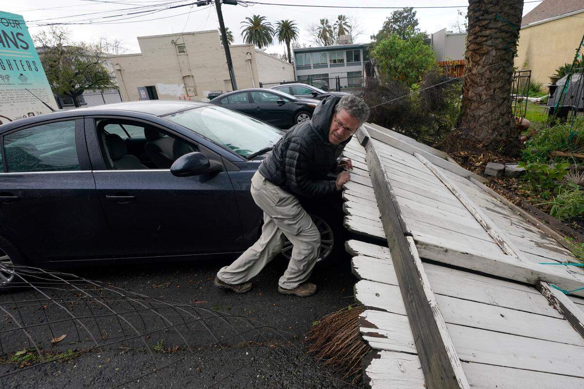 Bart Mehlhop lifts a fence blown over on a friends car by an overnight storm that swept through Sacramento, Calif., Wednesday, Jan. 27, 2021.