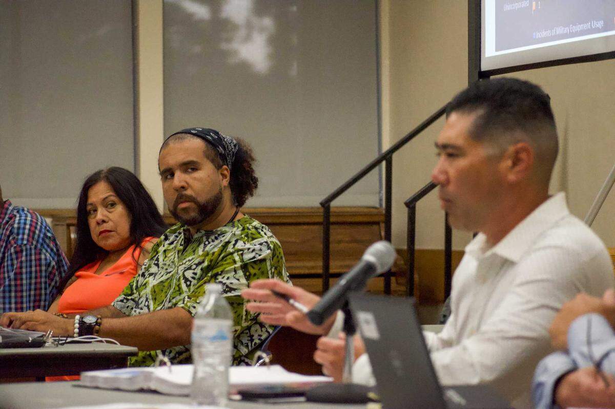 Ramona Landeros and Keyan Bliss listen as Lieutenant Jeff Shiraishi explains the police military usage report to the community on Monday, July 22, 2024. The meeting addressed concerns from the community around the use of military-equipment.