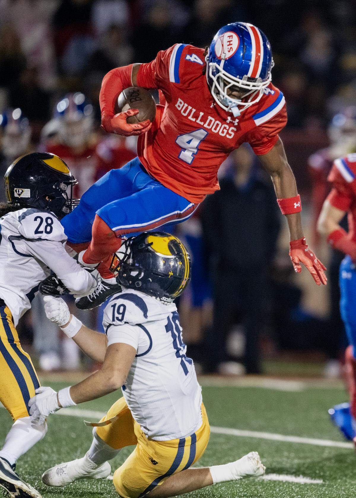 The Folsom Bulldogs' Isaiah Williams (4) is brought down by the Oak Ridge Trojans' Adrian Gallwitz (28) and Jonah Cedeno (19) in the first half of the CIF Sac-Joaquin Section football Division l championship on Friday, Nov. 28, 2025, at Hughes Stadium in Sacramento.